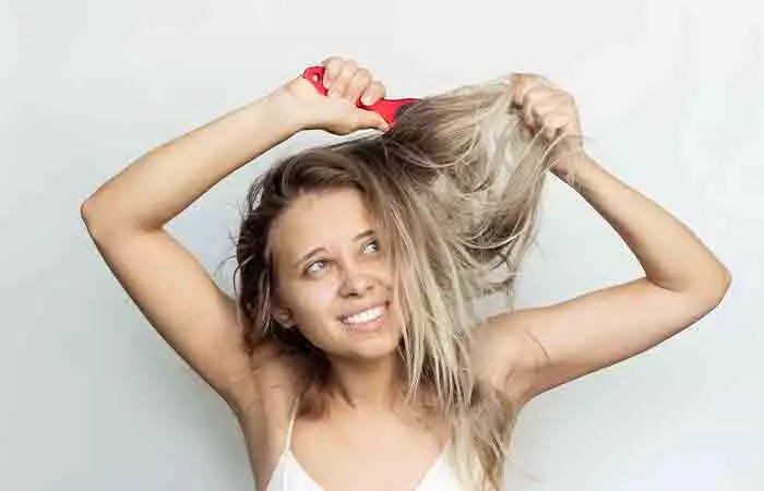 A girl is trying brush her damaged bleached hair.