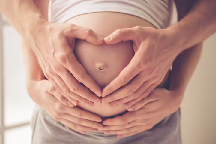 Making a heart on the bump with your own and partner's hands