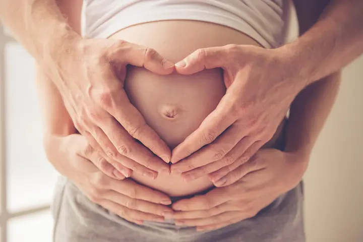 Making a heart on the bump with your own and partner's hands