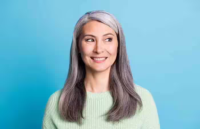 A woman with gray hair is smiling and looking away from the camera.