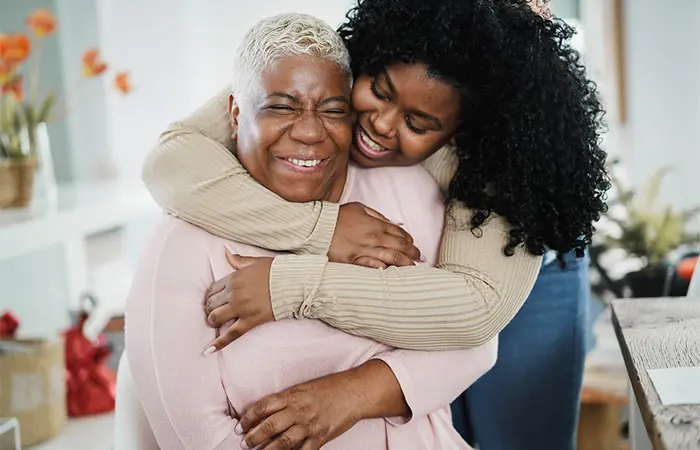 A girl hugging her mother from behind while they both smile out of happiness. 