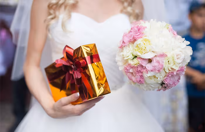 A bride holding a gift in one hand and a bouquet in another