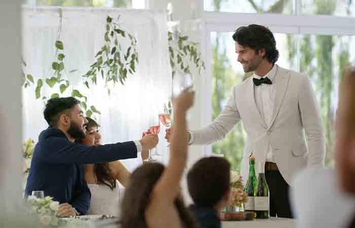 Man clinking glasses with bride and groom.