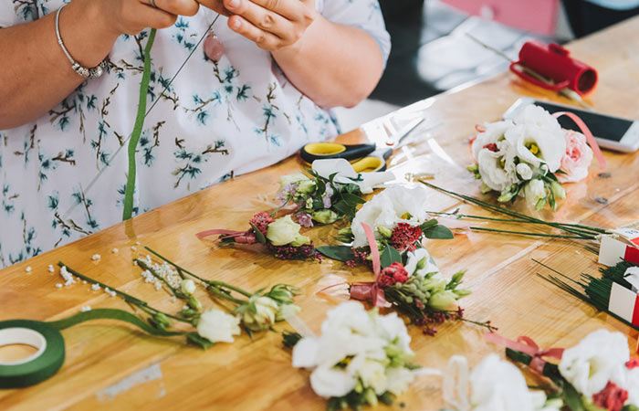 Person making a boutonniere with flowers, ribbon, and floral tape