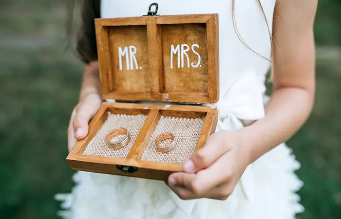 A girl carrying a beautiful box with rings under a Mr. and Mrs. sign